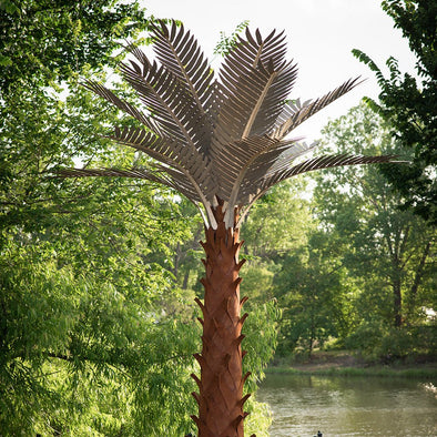 Metal Palm tree next to water and trees in background