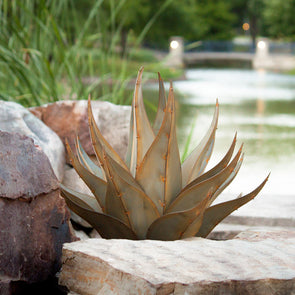 Metal agave with pond in background, next to landscape stones
