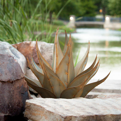 Metal agave with pond in background, next to landscape stones
